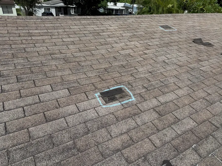 Shingle tabs torn off a roof by wind, the missing areas outlined in chalk, the street behind