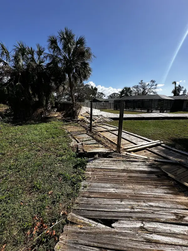 A wooden fence flattened by storm wind, palm trees behind